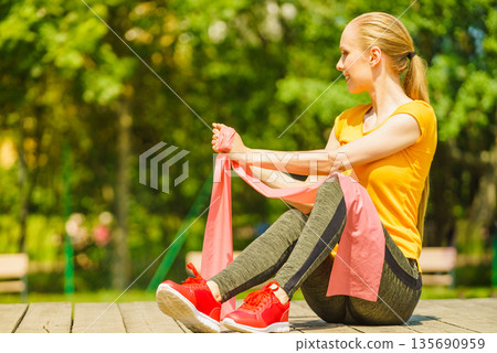 Girl doing exercise outdoor, using resistance fit band. Girl doing exercise outdoor, using resistance fit band. 135690959