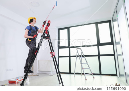 Worker elevates to paint ceiling in a bright modern room during daytime hours Worker elevates to paint ceiling in a bright modern room during daytime hours 135691090