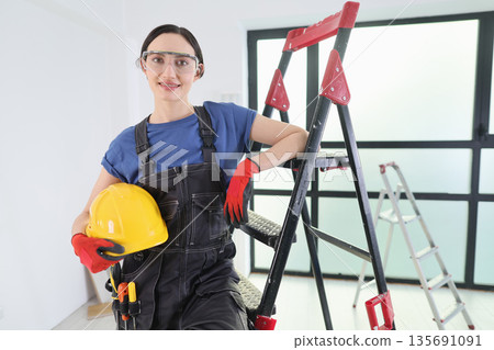 Dedicated woman in safety gear stands confidently next to a ladder while working on a home renovation project indoors Dedicated woman in safety gear stands confidently next to a ladder while working on a home renovation project indoors 135691091