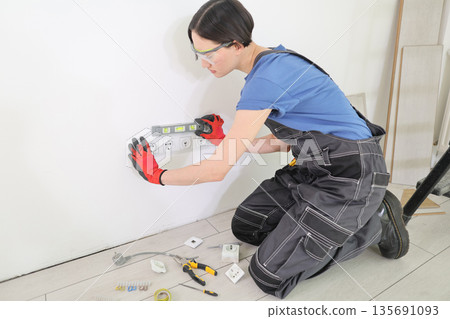 Skilled electrician working diligently on wall outlets in a bright, modern space during a DIY home renovation project 135691093
