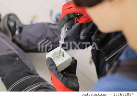 Electrician repairs a socket with precision in a modern workshop during daylight hours Electrician repairs a socket with precision in a modern workshop during daylight hours 135691094