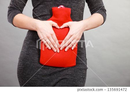 Girl holds hot water bottle on belly making heart shape by hands 135691472