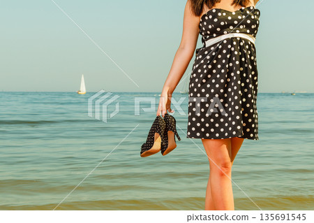 Woman in retro dress holding shoes near sea 135691545