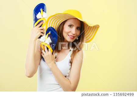 Woman in big yellow summer hat holds flip flops Woman in big yellow summer hat holds flip flops 135692499