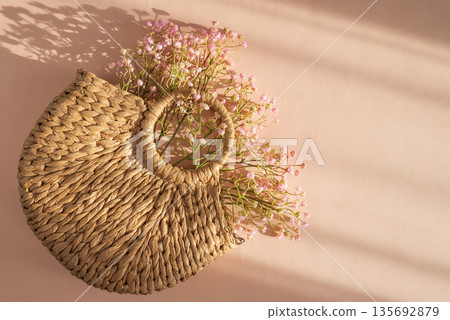 Woven Straw Handbag with Flowers. Elegant Summer Fashion Flatlay on Peach Background Woven Straw Handbag with Flowers. Elegant Summer Fashion Flatlay on Peach Background 135692879