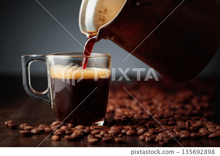 Black coffee is poured into a glass cup. 135692898