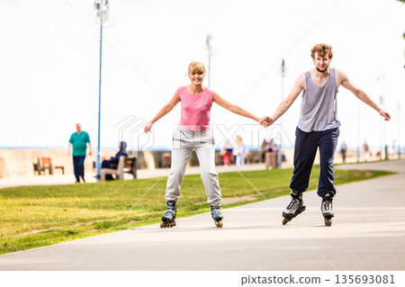 Young couple rollerblading in park holding hands. 135693081