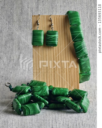 Set of handmade jewelry consisting of beads, earrings and a bracelet made of green malachite on a burlap background on a wooden stand 135693118