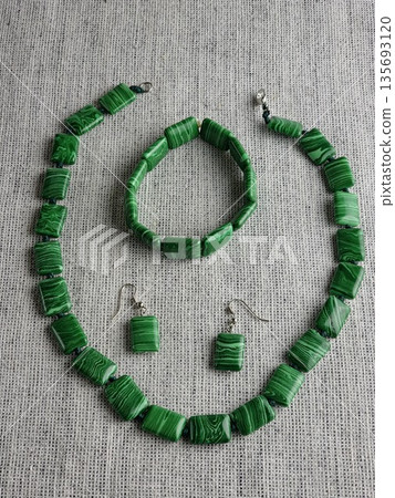 Handmade set of beads, earrings and bracelet made of green malachite on a burlap background 135693120