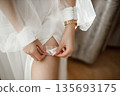 Bride putting on wedding garter before ceremony 135693175