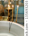 Golden cross hanging on baptismal font between three candles 135693203