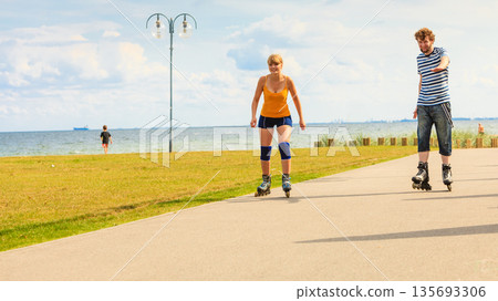 Young couple on roller skates riding outdoors Young couple on roller skates riding outdoors 135693306