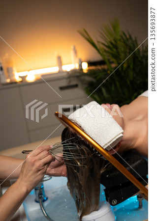 Woman receiving a relaxing head spa treatment with flowing water and professional scalp massage in a wellness salon. Woman receiving a relaxing head spa treatment with flowing water and professional scalp massage in a wellness salon. 135693877