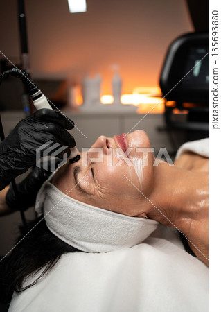 Senior woman receiving professional RF lifting facial treatment focused on skin tightening and age-related skincare. Senior woman receiving professional RF lifting facial treatment focused on skin tightening and age-related skincare. 135693880