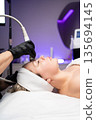 Woman receiving noninvasive radiofrequency facial treatment for skin tightening and rejuvenation in a medical spa. 135694145