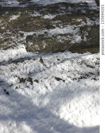 Snow Covers a Stone Wall With a Rough Texture in a Cold Outdoor Setting 135694201