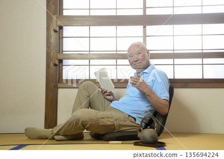 An elderly man enjoying reading in a Japanese-style room 135694224