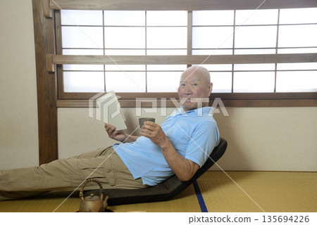 一位老人在日式房間裡享受閱讀的樂趣。 一位老人在日式房間裡享受閱讀的樂趣。 135694226