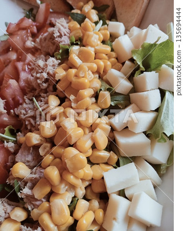 Close-up of a fresh mixed salad with tuna, corn, tomatoes, and diced cheese 135694444