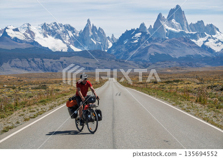 Cyclist riding straight road toward massive Mount Fitz Roy, Patagonia, Argentina Cyclist riding straight road toward massive Mount Fitz Roy, Patagonia, Argentina 135694552