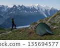 Hiker standing by tent viewing Mont Blanc massif and Bossons Glacier, France 135694577