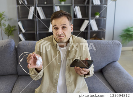 Closeup of man with phone and charger, confused by charging failure at home 135694812