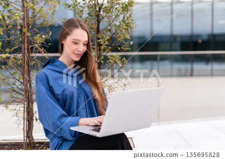 Smiling businesswoman using laptop near modern Smiling businesswoman using laptop near modern 135695828