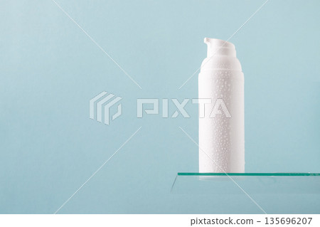 White cosmetic pump bottle on glass shelf with water drops on blue background 135696207