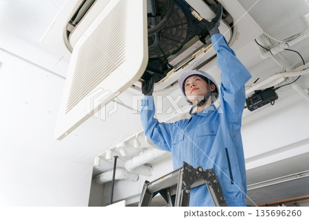 A female worker inspecting an air conditioner A female worker inspecting an air conditioner 135696260
