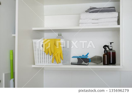 Organizing cleaning supplies and towels on white cabinet shelves 135696279