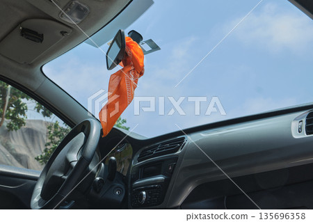 Orange bandana hanging from car rear view mirror 135696358