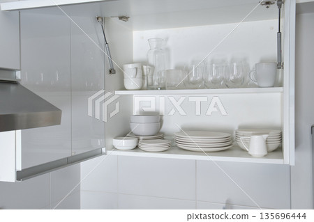 White kitchen cabinet storing organized minimalist dishes and glassware White kitchen cabinet storing organized minimalist dishes and glassware 135696444