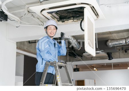 A female worker inspecting an air conditioner 135696470