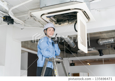 A female worker inspecting an air conditioner 135696471