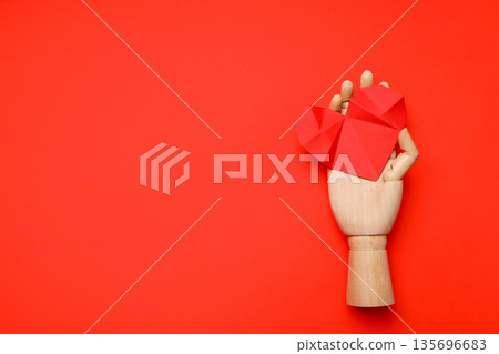 Wooden hand holds red paper hearts on a bright backdrop Wooden hand holds red paper hearts on a bright backdrop 135696683