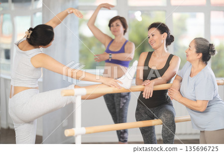 Relaxed women casually socializing at ballet barre in studio 135696725