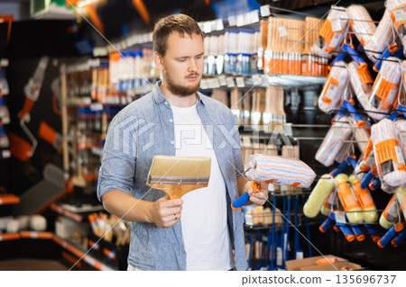 Young man choose brush and painting roller and selects desired option 135696737