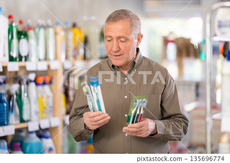 Mature male shopper chooses best toothbrush and toothpaste in supermarket Mature male shopper chooses best toothbrush and toothpaste in supermarket 135696774