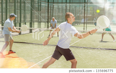 Adult and young men playing padel against two men 135696775