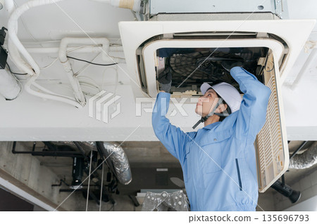 A female worker inspecting an air conditioner 135696793