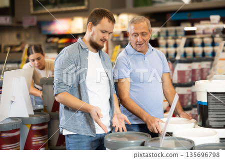 Hardware store clerk offers an elderly male customer can of paint 135696798