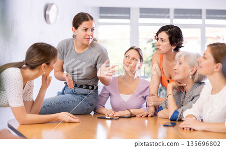 young girl student sits on table near friends and promotes version of solution of educational task young girl student sits on table near friends and promotes version of solution of educational task 135696802