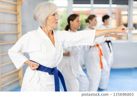 Elderly woman in white kimono performing kata routines at karate training Elderly woman in white kimono performing kata routines at karate training 135696803