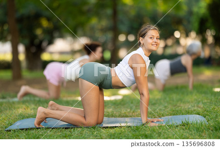 Girl performing Bitilasana Marjaryasana during group yoga in park Girl performing Bitilasana Marjaryasana during group yoga in park 135696808