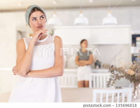 Offended mother standing in the kitchen with her back to upset young daughter Offended mother standing in the kitchen with her back to upset young daughter 135696818