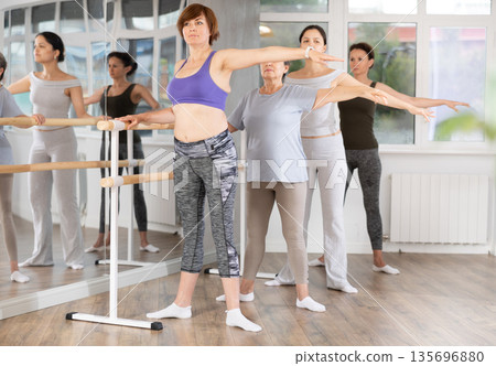 Mature woman practicing second position in amateur group ballet class Mature woman practicing second position in amateur group ballet class 135696880