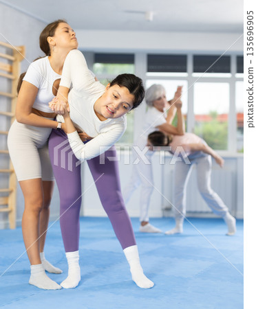 Asian woman escaping from back grip and striking to chin with elbow during self-defense training 135696905
