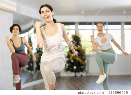 Young woman energizing female group during dance workout in Christmas studio Young woman energizing female group during dance workout in Christmas studio 135696929