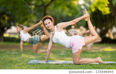 Happy sporty skilled young women going table pose of yoga with group in park at daytime 135696944
