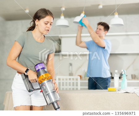 Girl collects dust with vacuum cleaner during group cleaning in kitchen 135696971